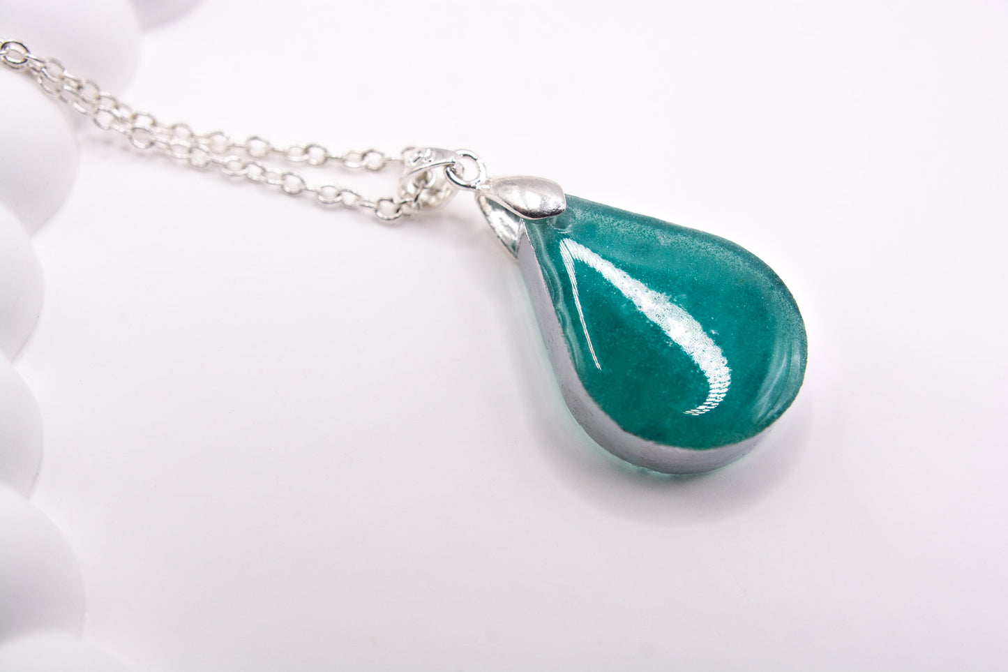 A view of the back of a teal teardrop shaped cremation ashes memorial keepsake pendant, set on a 925 sterling silver chain 