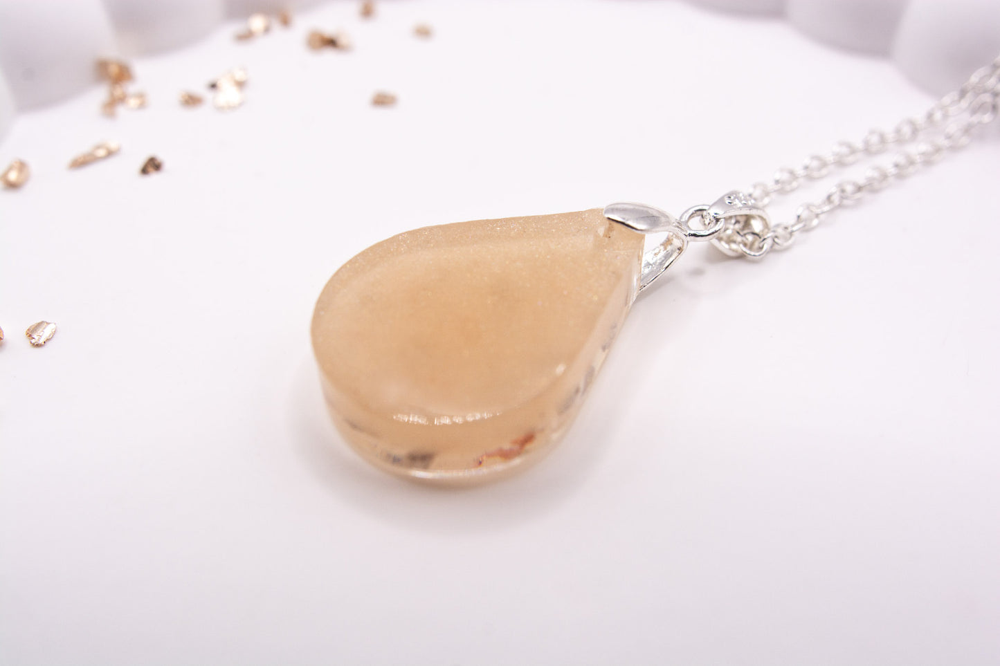 The back view of a metallic cream teardrop shaped keepsake memorial pendant set on a 925 sterling silver chain