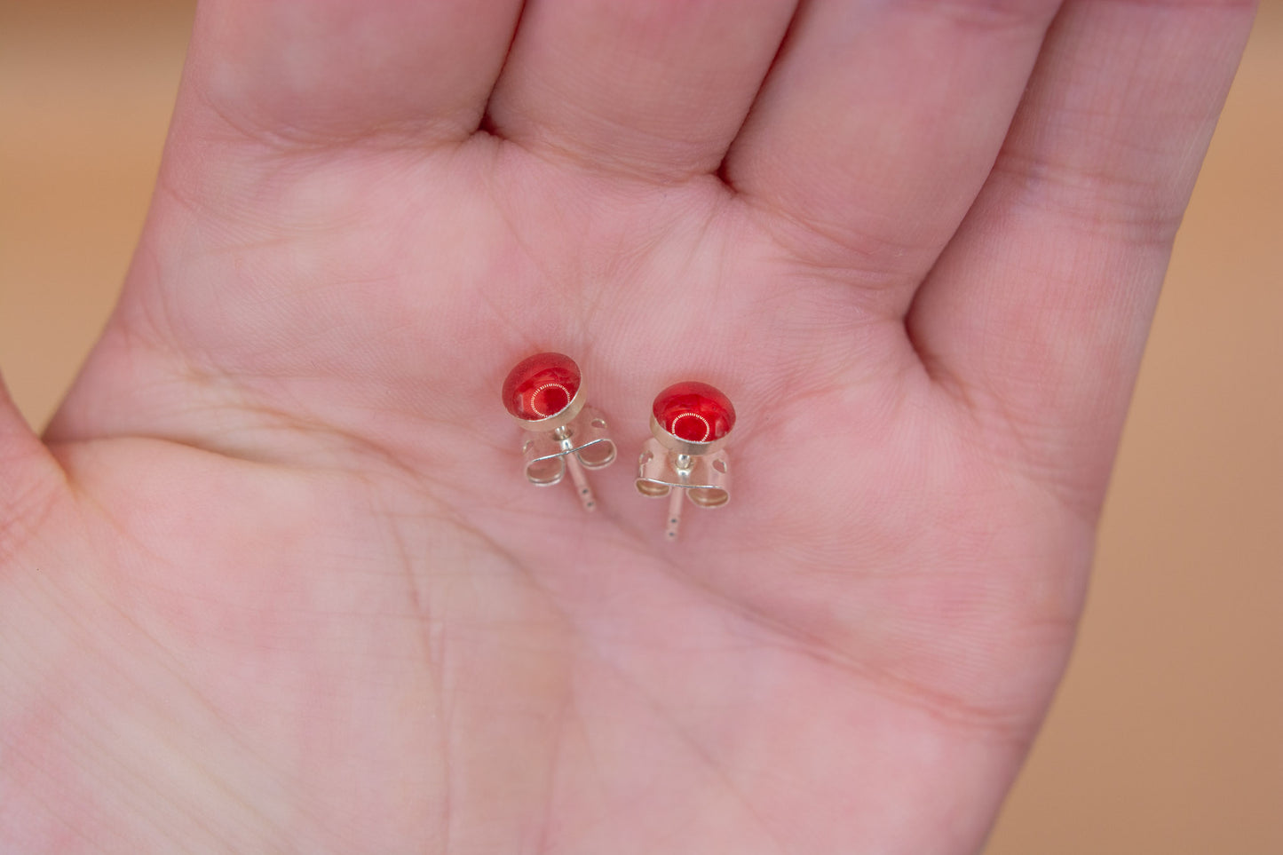 A close up shot of a pair of cherry red cremation ashes stud earrings in 925 silver, presented in the palm of a hand