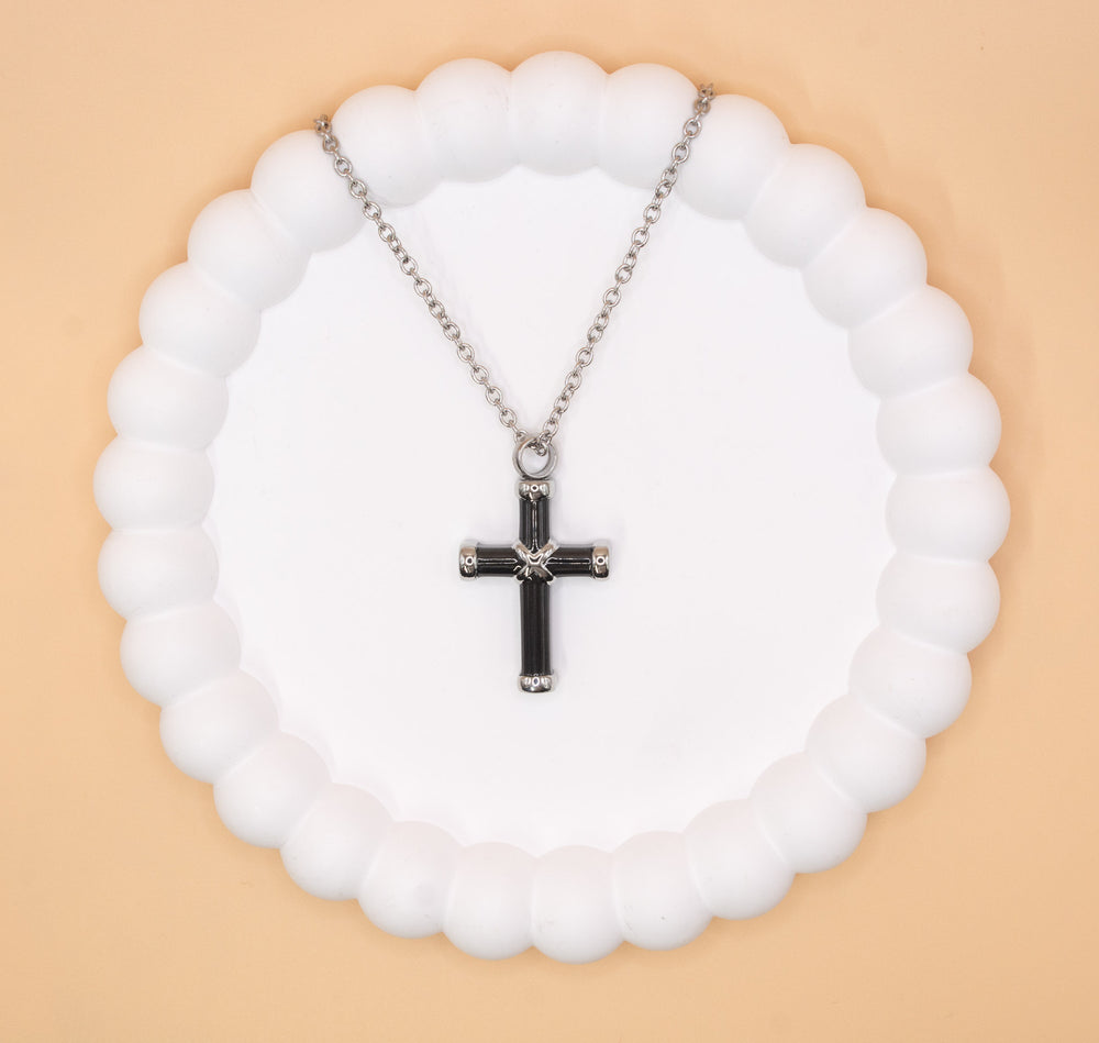 An aerial overhead view of a black and silver stainless steel cross pendant, which is ideal for any gender. It can be self-filled with cremation ashes or sand from a loved ones favourite beach