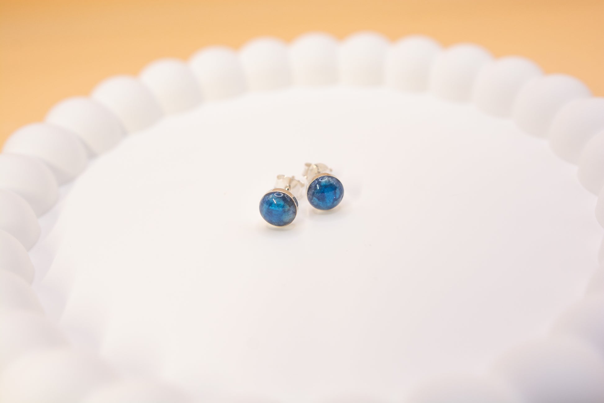 A close up shot of a pair of 925 silver stud earrings, cobalt blue in colour, made with cremation ashes. presented on a white ceramic jewellery tray