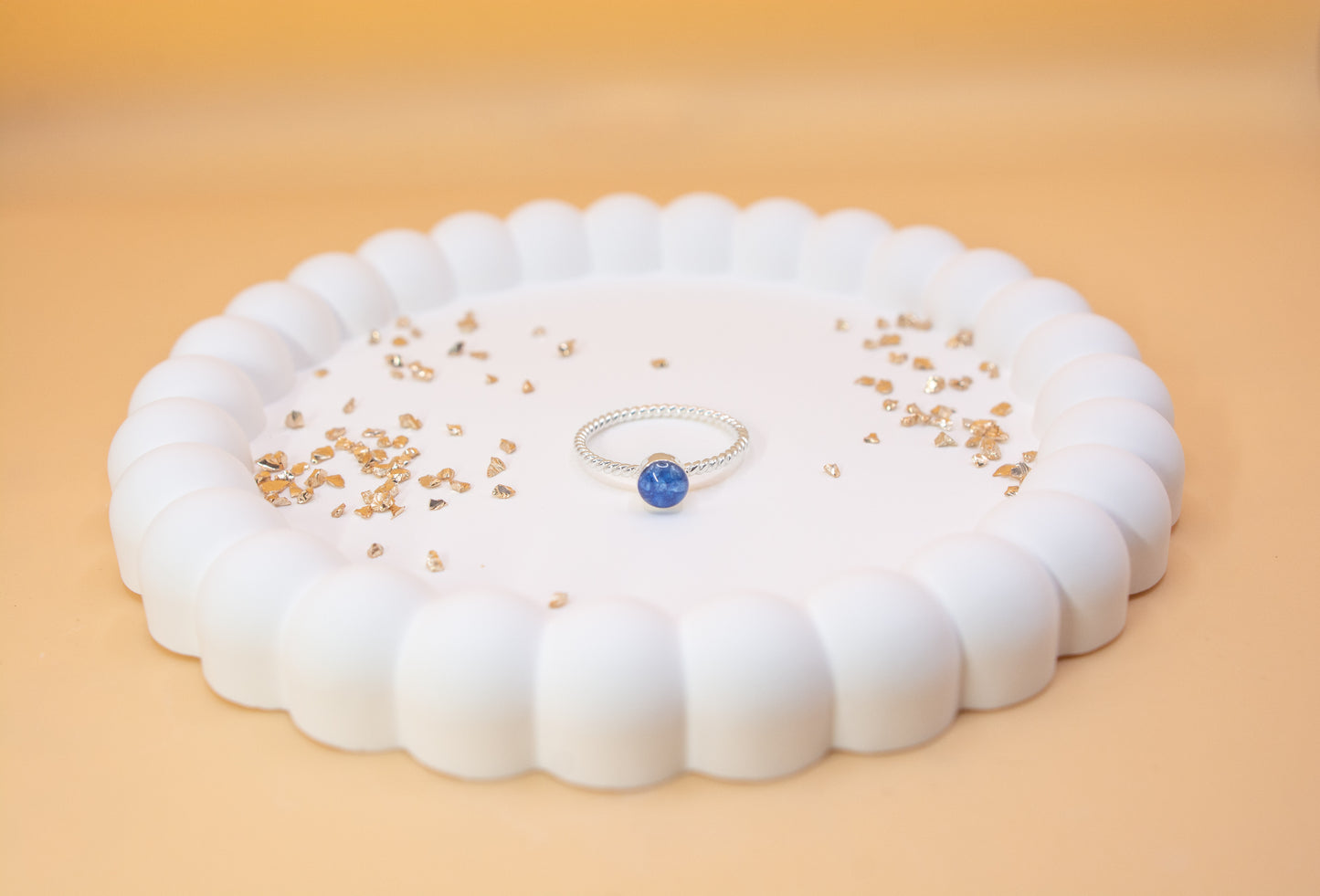 A 925 silver twist design ring, in cobalt blue colour, which contains cremation ashes, displayed on a jewelry plate with gold sparkles either side of it