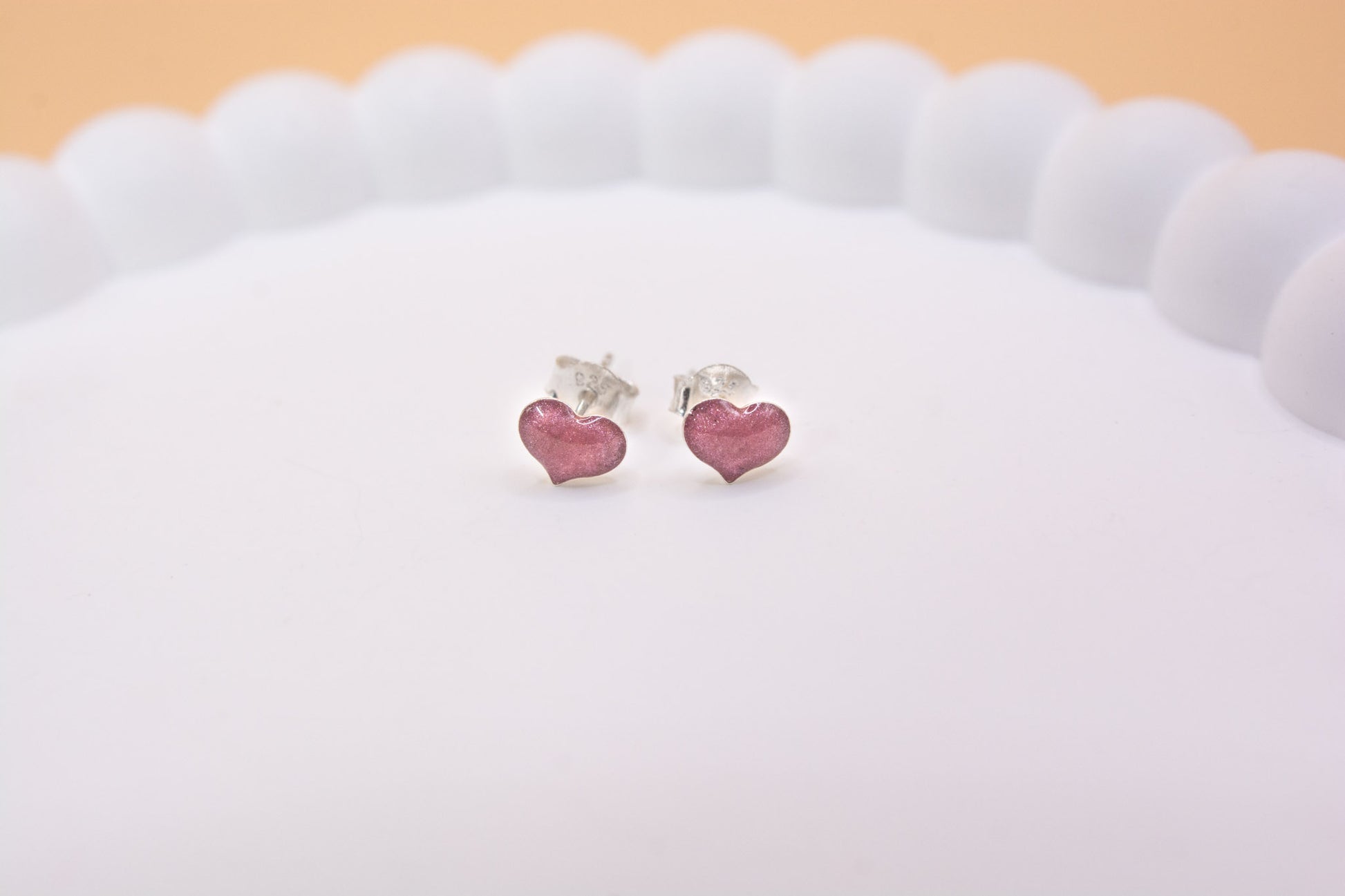 A close up view of a pair metallic dusty pink coloured heart shaped stud earrings, containing cremation ashes, made in 925 sterling silver