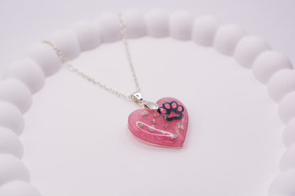 A close up angled view of a pink Heart shaped keepsake memorial pendant, set on a 925 sterling silver chain, containing a paw print decal and pet cremation ashes