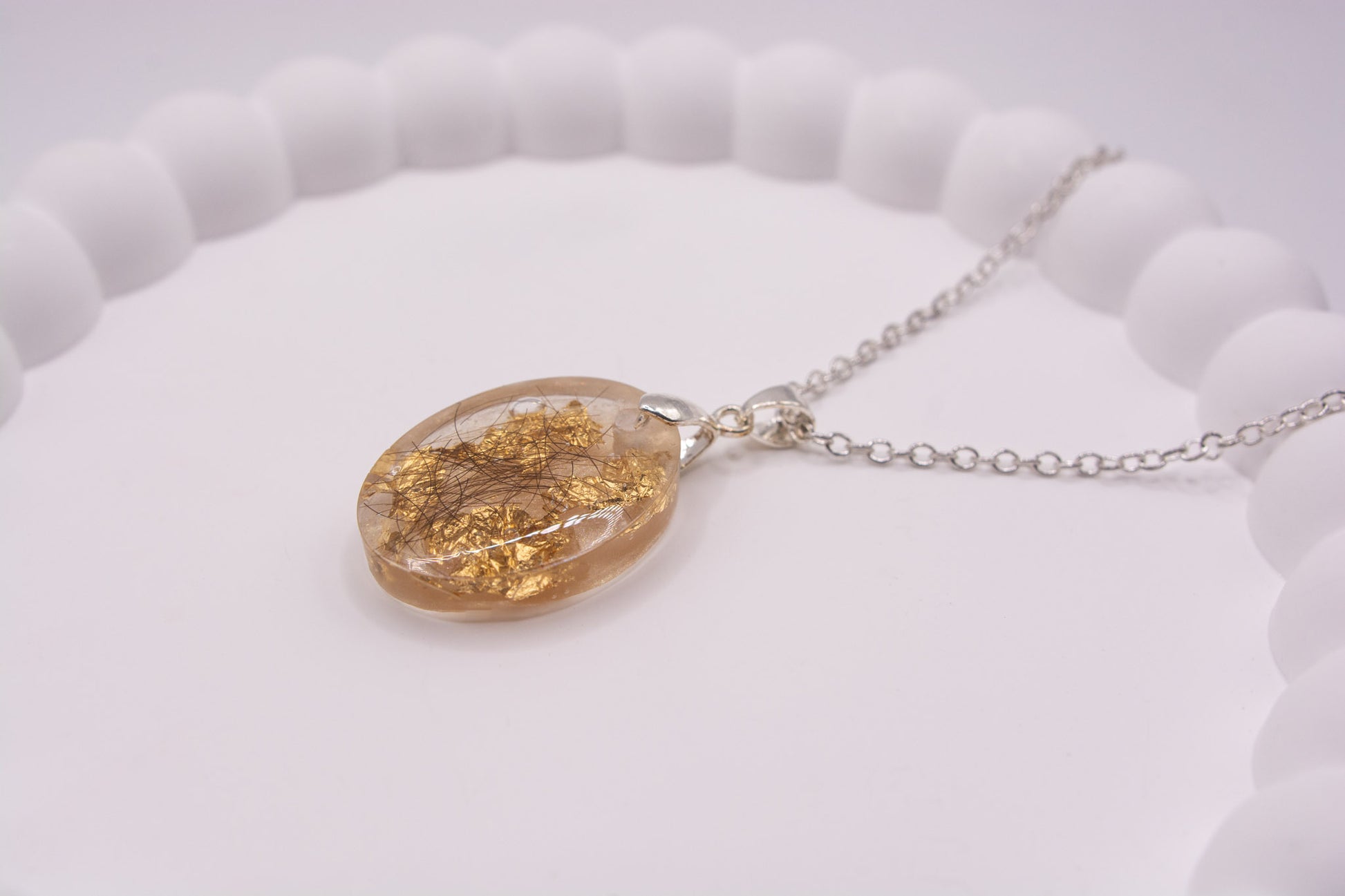 Angled side view of a clear oval shaped keepsake memorial pendant, containing gold flake and human hair, set on a 925 sterling silver chain