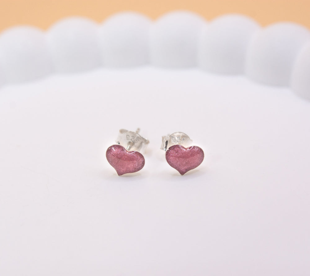 A close up shot of a pair of 925 sterling silver, pink coloured heart shaped stud earrings, containing cremation ashes