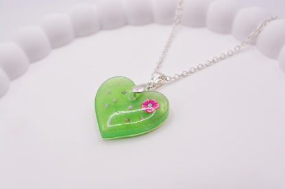 A close up angled view of a green heart keepsake memorial pendant, containing a flower decoration and cremation ashes, set on a 925 sterling silver chain