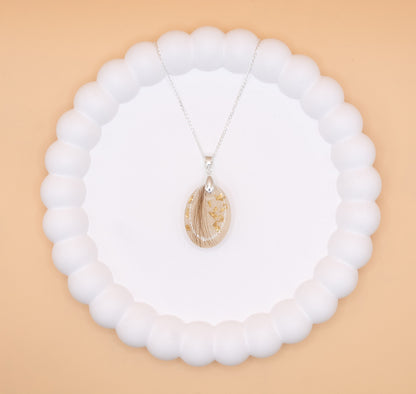 An aerial view of an oval shaped pendant containing a lock of hair and gold flakes, set on a 925 silver necklace chain, presented on a jewelry display tray