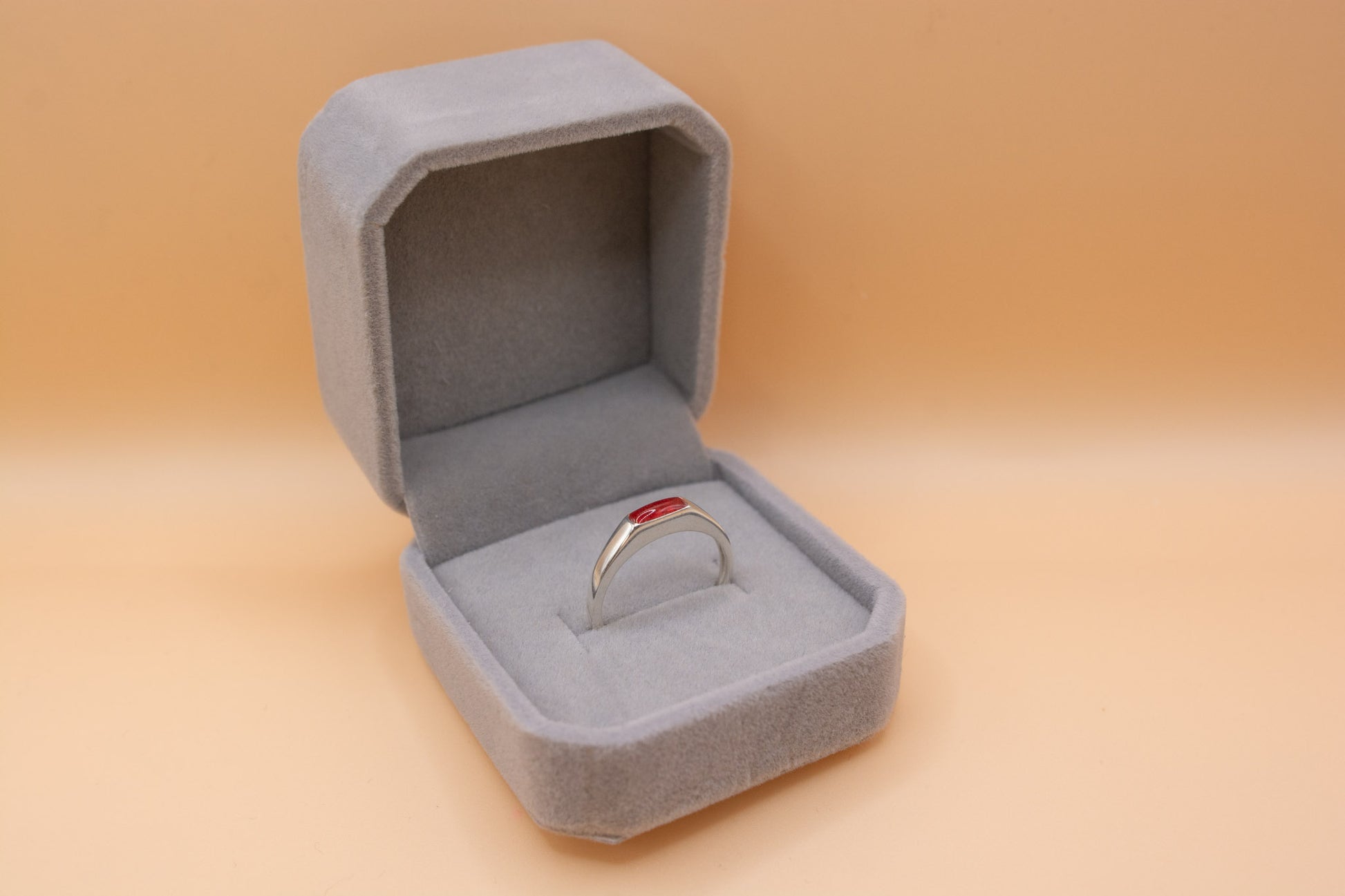 An angled view of a plush grey ring box, containing a solid 925 silver ring, which has a rectangular bezel containing cherry red resin and cremation ashes