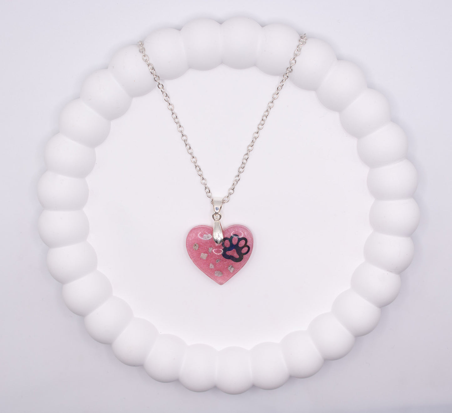 An aerial overhead view of a pink Heart shaped keepsake memorial pendant, set on a 925 sterling silver chain, containing a lost loved pet dog's cremation ashes