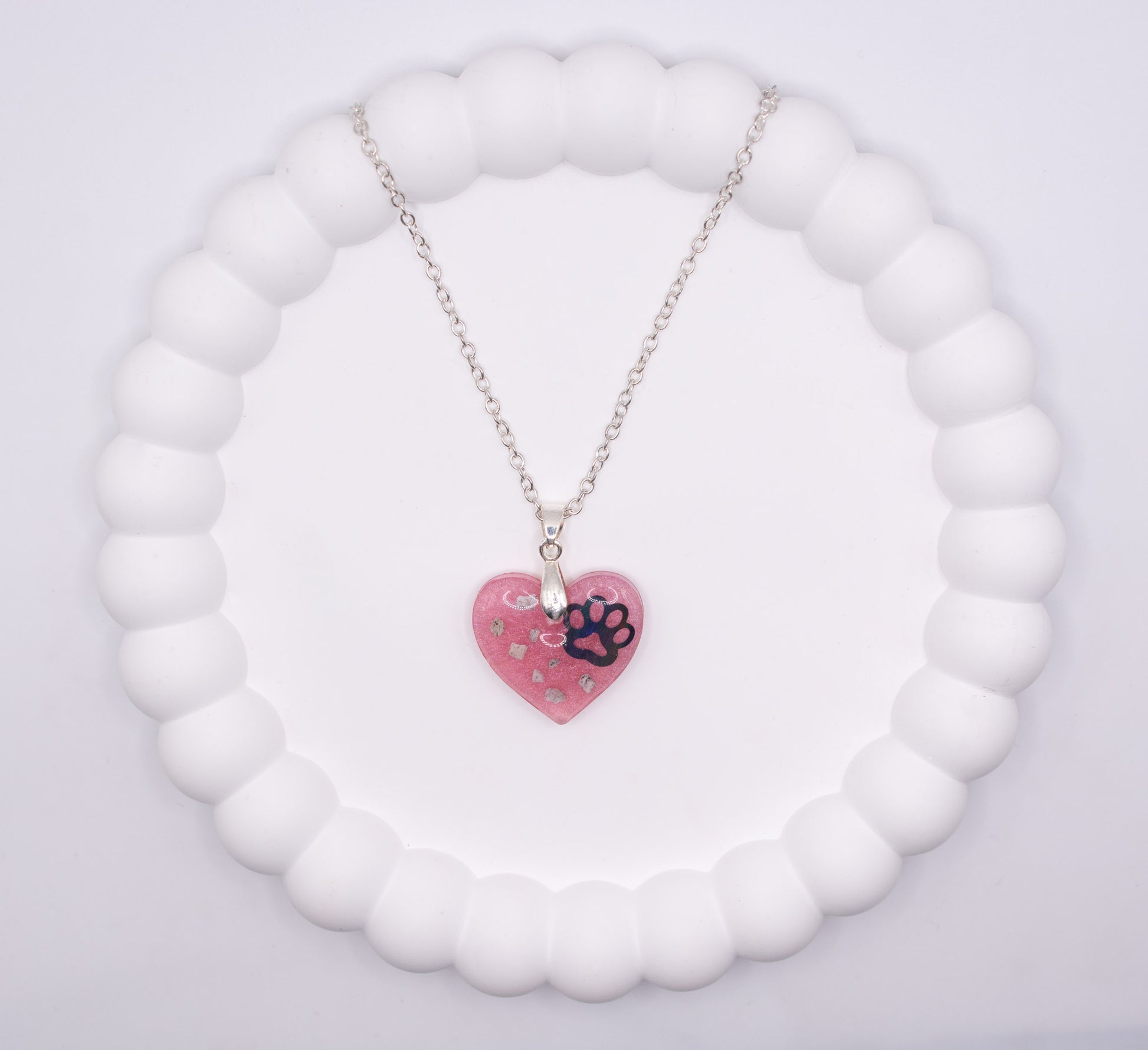 An aerial overhead view of a pink Heart shaped keepsake memorial pendant, set on a 925 sterling silver chain, containing a lost loved pet dog's cremation ashes