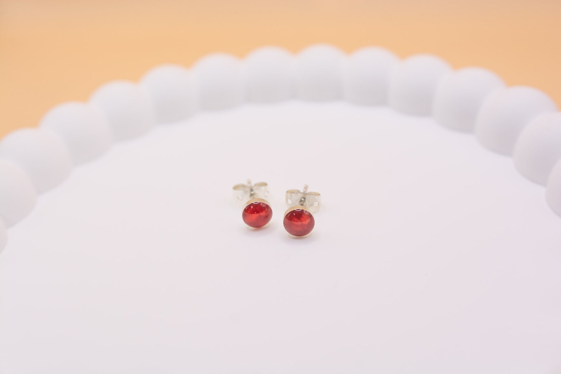 A close-up front view of a pair of memorial stud earrings, containing red resin and lost beloved pet ashes. Made in 925 silver.