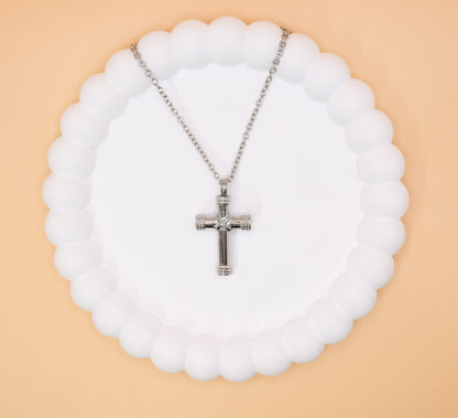 An aerial view of a silver coloured stainless steel cross pendant, ideal for any gender. It can be self-filled with cremation ashes or sand from a loved ones favourite beach