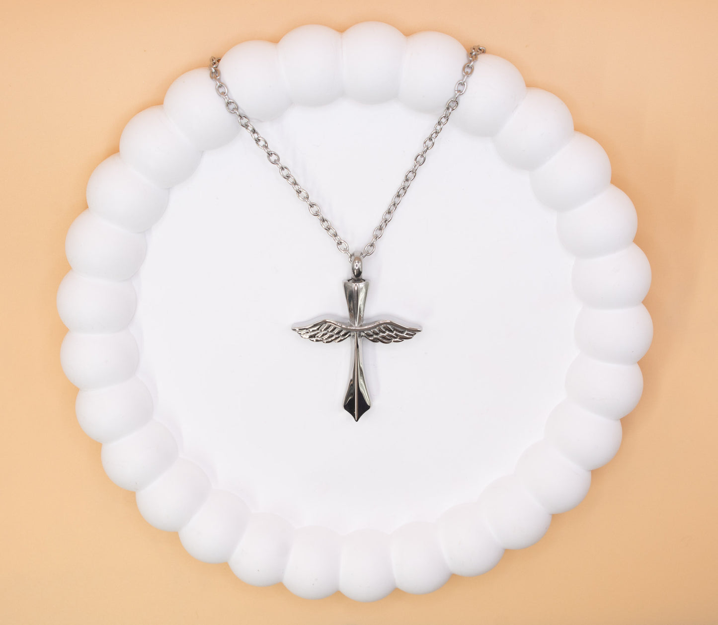 An aerial view of a beautiful stainless steel cross with angel wings pendant, which can be self-filled with cremation ashes or sand from the beach