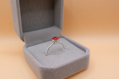 An angled, close-up view of a keepsake memorial twist ring, in 925 silver, containing red resin and cremation ashes