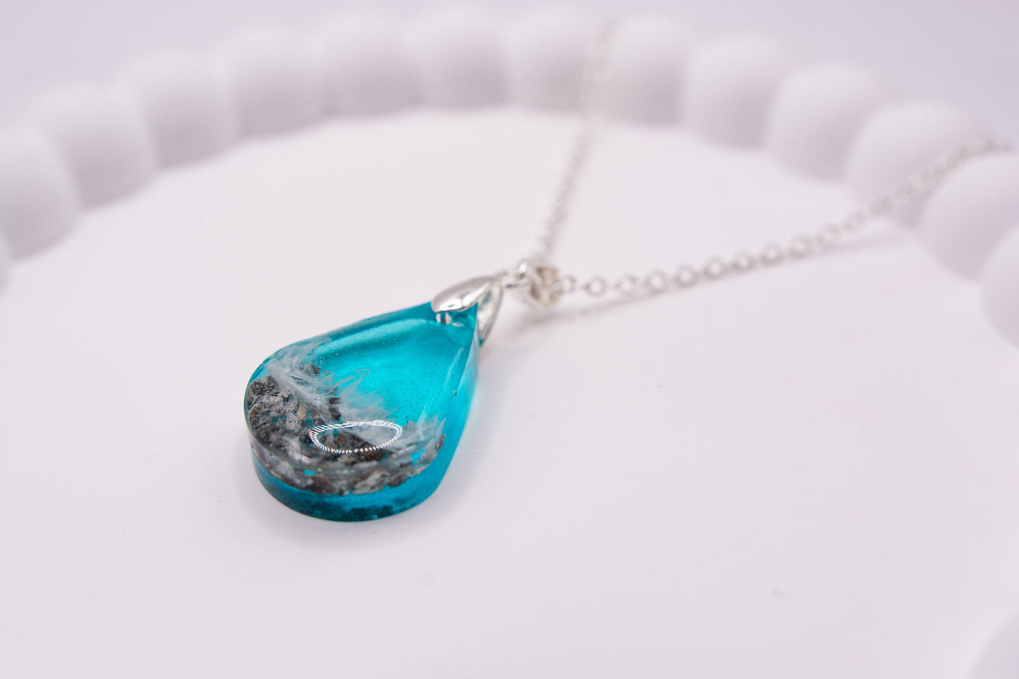 A closer up angled view of a Teardrop shaped seashore memorial keepsake pendant, containing cremation ashes and beach sand, on a sterling 925 silver chain